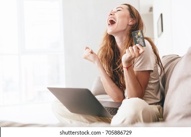 Šťastná mladá žena s kreditní kartou a notebookem sedí na pohovce doma Stock fotografie