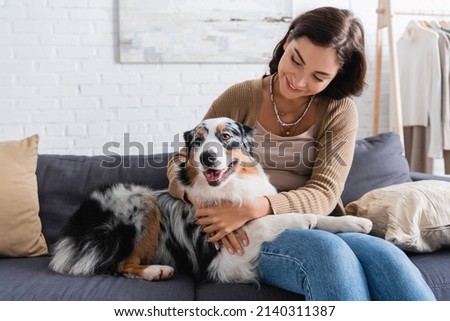 happy young woman cuddling australian shepherd dog while sitting on couch