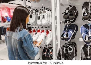 Happy Young Woman Customer Choosing Pair Of Sneakers Shoes And Buying It In Clothes Store, Casual Shopping Concept