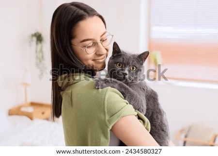 Happy young woman with cute British Shorthair cat in bedroom, closeup