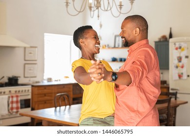 Happy Young Woman Dance With Her Husband As They Celebrate A Special Day At Home. Young African Couple Dancing And Laughing At New Home. Mature Couple Having Fun Together While Dancing In Kitchen.