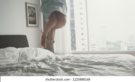 Happy young woman dancing, jumping on bed at home having fun in the bed in a luxury apartment with city view in Malaysia