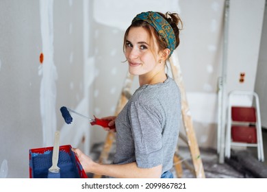 Happy young woman decorating the walls her apartment turning to look over her shoulder at the camera and friendly smile