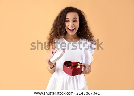 Happy young woman with delicious chocolate candies in box on color background