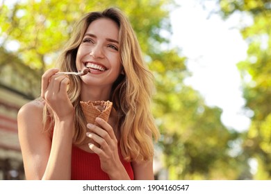 Happy young woman with delicious ice cream in waffle cone outdoors. Space for text - Powered by Shutterstock