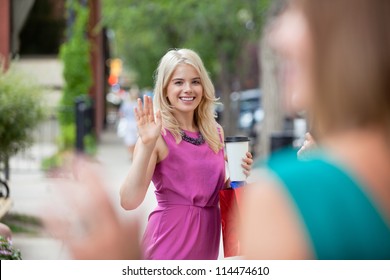 Happy young woman with disposable coffee cup waving to female friend