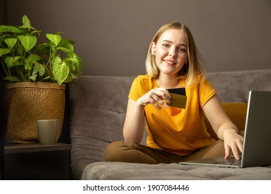 Happy Young Woman Do Online Shopping, Ordering Delivery Using Laptop. Teenager Girl Makes Purchases Online Using Credit Bank Card Relax On Sofa At Home Interior. Mockup Blank For Credit Bank Card