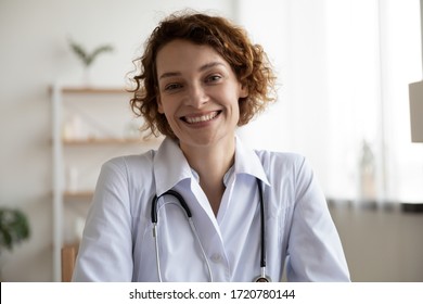 Happy young woman doctor wears white medical coat and stethoscope looking at camera. Smiling female physician, general practitioner consult patient online by video call. Close up head shot portrait