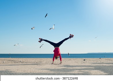 Happy young woman doing cartwheel on the beach wearing rollerskates. Portrait of woman on the beach doing a handstand with sea and seagulls in background.
 - Powered by Shutterstock