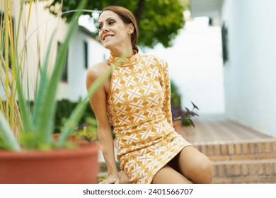 Happy young woman in dress sitting near blurred aloe vera plant in daylight - Powered by Shutterstock