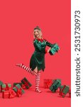 Happy young woman dressed as elf with Christmas gifts on red background