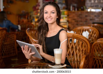 Happy Young Woman Drinking Coffee / Tea And Using Tablet Computer In A Coffee Shop