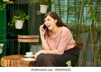 Happy Young Woman Drinking Cup Of Coffee In Her Backyard And Talking On Phone With Friend Or Family Member