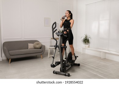 Happy young woman drinking water during training on elliptical machine at home - Powered by Shutterstock