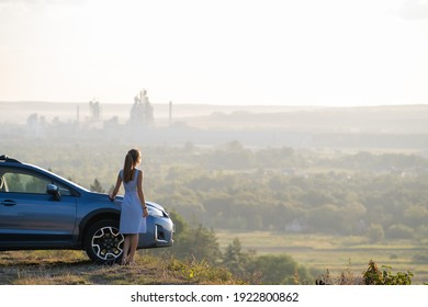 Fröhliche junge Frau Fahrer in blauem Kleid genießen warmen Sommerabend neben ihrem Auto stehen. Reise- und Urlaubskonzept.