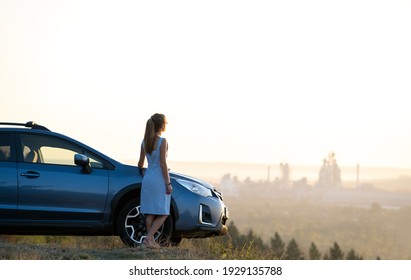 Happy young woman driver in blue dress leaning on her car enjoying warm summer day. Travelling and vacation concept.