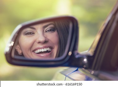 Happy Young Woman Driver Looking In Car Side View Mirror, Making Sure Lane Is Free Before Making A Turn. Positive Human Face Expression Emotions. Safe Trip Driving Concept