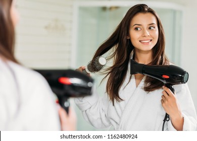 Happy Young Woman Drying Hair At Mirror In Bathroom 