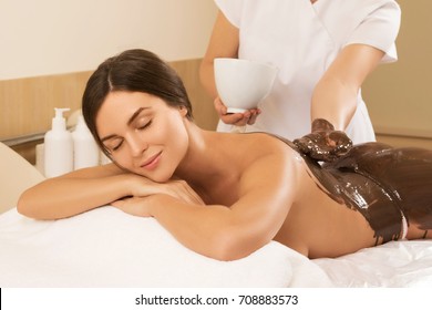 Happy Young Woman During A Chocolate Wrap Or Massage In Spa Salon