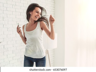 Happy Young Woman In Earphones Is Listening To Music With Smart Phone, Dancing And Smiling