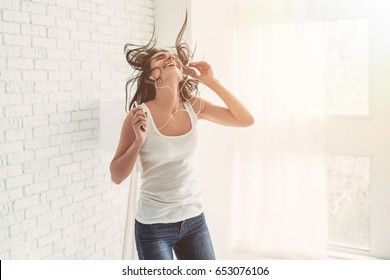 Happy young woman in earphones is listening to music with smart phone, dancing and smiling