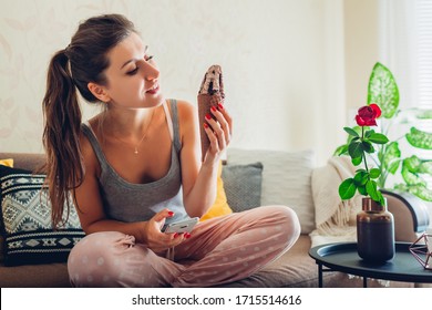 Happy Young Woman Eating Chocolate Ice-cream In Cone Lying On Couch At Home And Using Smartphone. Relaxing In Living Room Enjoying Dessert