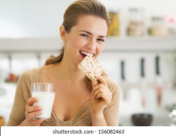 Happy Young Woman Eating Crisp Bread With Milk In Kitchen