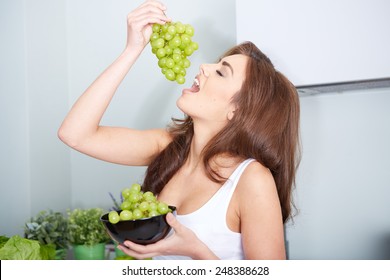 Happy young woman eating grapes in a kitchen