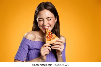 Happy young woman eating pizza, posing with slice and giggle coquettish, biting food, concept of fast food restaurants, pizzeria, standing over orange background