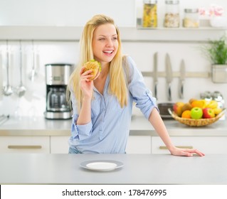 Happy Young Woman Eating Sandwich In Kitchen