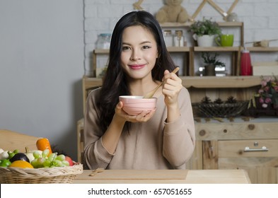 Happy young woman eating soup in kitchen