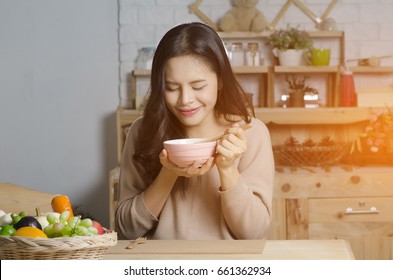 Happy Young Woman Eating Soup In Kitchen