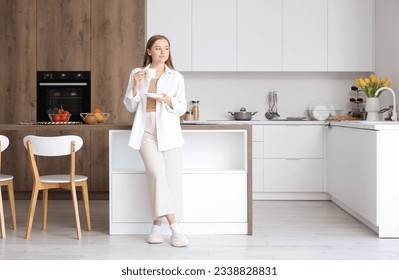 Happy young woman enjoying cup of coffee in modern kitchen - Powered by Shutterstock