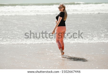 Happy young woman enjoying sunny days on the beach. Portrait beautiful girl walking and playing with sand. Smiling blond female posing near ocean. Vacation in Portugal