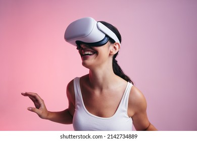 Happy young woman entering a fun virtual reality game in a studio. Woman laughing cheerfully while wearing a virtual reality headset. Female gamer exploring 3D technology. - Powered by Shutterstock