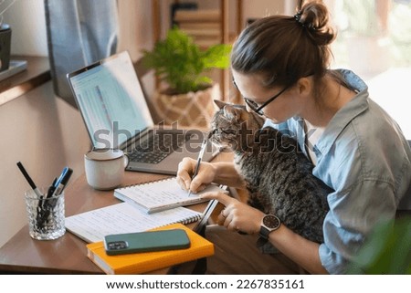 Happy young woman in eyeglasses  works at home  with a laptop and a cat, remote work and education