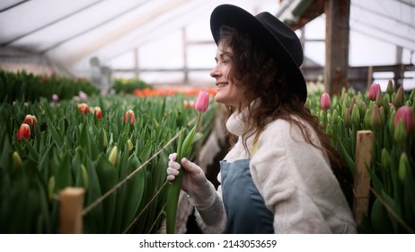 Happy young woman farmer in a hat sings song with tulip flower while working in a greenhouse