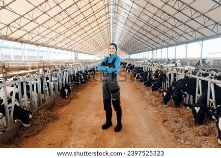 Happy young woman farmer in uniform against background of hangar barn with cows. Concept livestock agriculture industry.