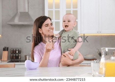 Happy young woman feeding her cute little baby at table in kitchen