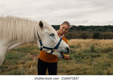 Happy young woman feeding horse with apple from hand in outdoors. - Powered by Shutterstock