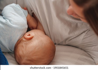 happy young woman feeds breast milk and hugs baby. a mother is breastfeeding a newborn baby while lying on the bed. Concept of newborn lactation. The child eats milk before going to bed. Side view.