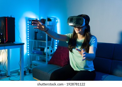 Happy young woman feeling excited while using virtual reality glasses and having fun while sitting on the couch of her bedroom