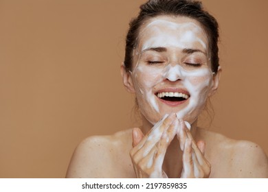 Happy Young Woman With Foaming Face Wash Washing Face Against Beige Background.