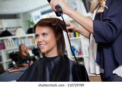 Happy young woman getting her hair set by beautician after the new haircut