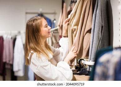 Happy Young Woman Girl Chooses Beige Knitwear Clothes For Autumn Or Winter In Clothing Store. Shopping In Shop.