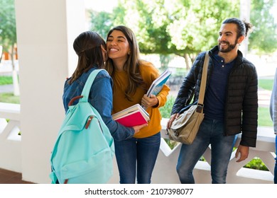 Happy young woman giving a kiss on the cheek to her best friend at the university while carrying books to class