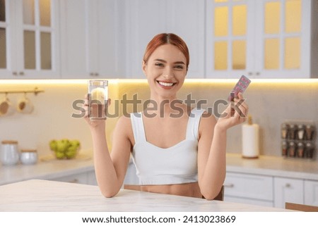 Happy young woman with glass of water and pills at table in kitchen. Weight loss
