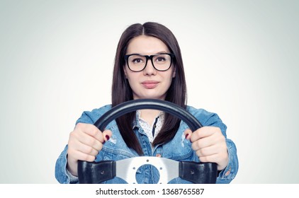 Happy young woman with glasses and car steering wheel, front view, auto concept 