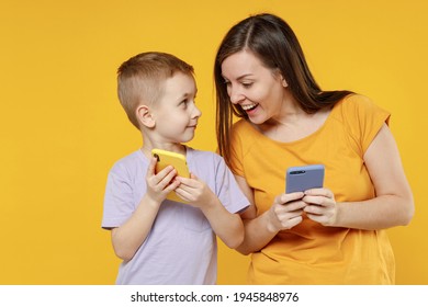 Happy Young Woman Have Fun With Child Baby Boy 5-6-7 Years Old In Violet T-shirt Hold Use Mobile Cell Phone. Mommy Little Kid Son Together Isolated On Yellow Background Studio Mother's Day Love Family