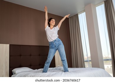 Happy young woman having fun and dancing on the bed in the bedroom. Bottom view. Indoor.